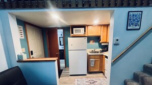 A compact kitchen with wooden cabinets, a white refrigerator, and a microwave. A patterned rug is on the floor, and a wooden staircase leads to another room. - Valdez Robe River Front Property (Valdez)