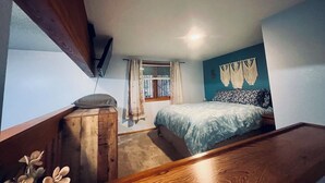 A bedroom with a bed, a window with curtains, a wall-mounted TV, and a wooden headboard. - Valdez Robe River Front Property (Valdez)