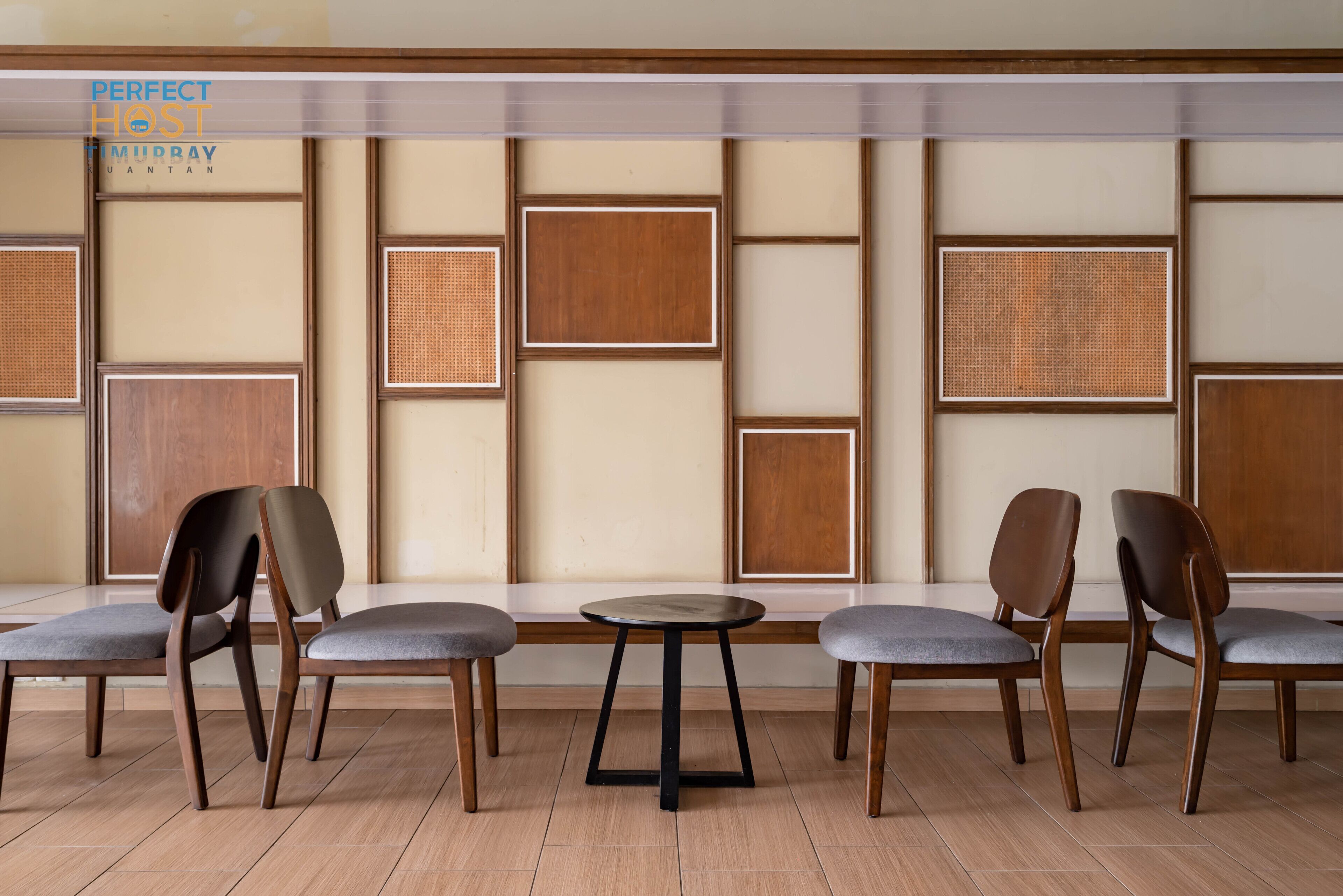 Angolo salotto con sedie in legno e un tavolino rotondo, con un muro in stile asiatico caratterizzato da pannelli e tappeti tessuti.