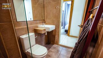 A bathroom with a toilet, sink, and mirror. There is a towel rack with a towel hanging on it.