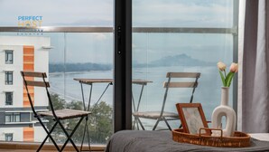 A hotel room with a large window, a bed, two wooden chairs, a wicker basket with a picture frame and a vase with flowers. - Timurbay beachfront by Perfect Host (Kuantan)