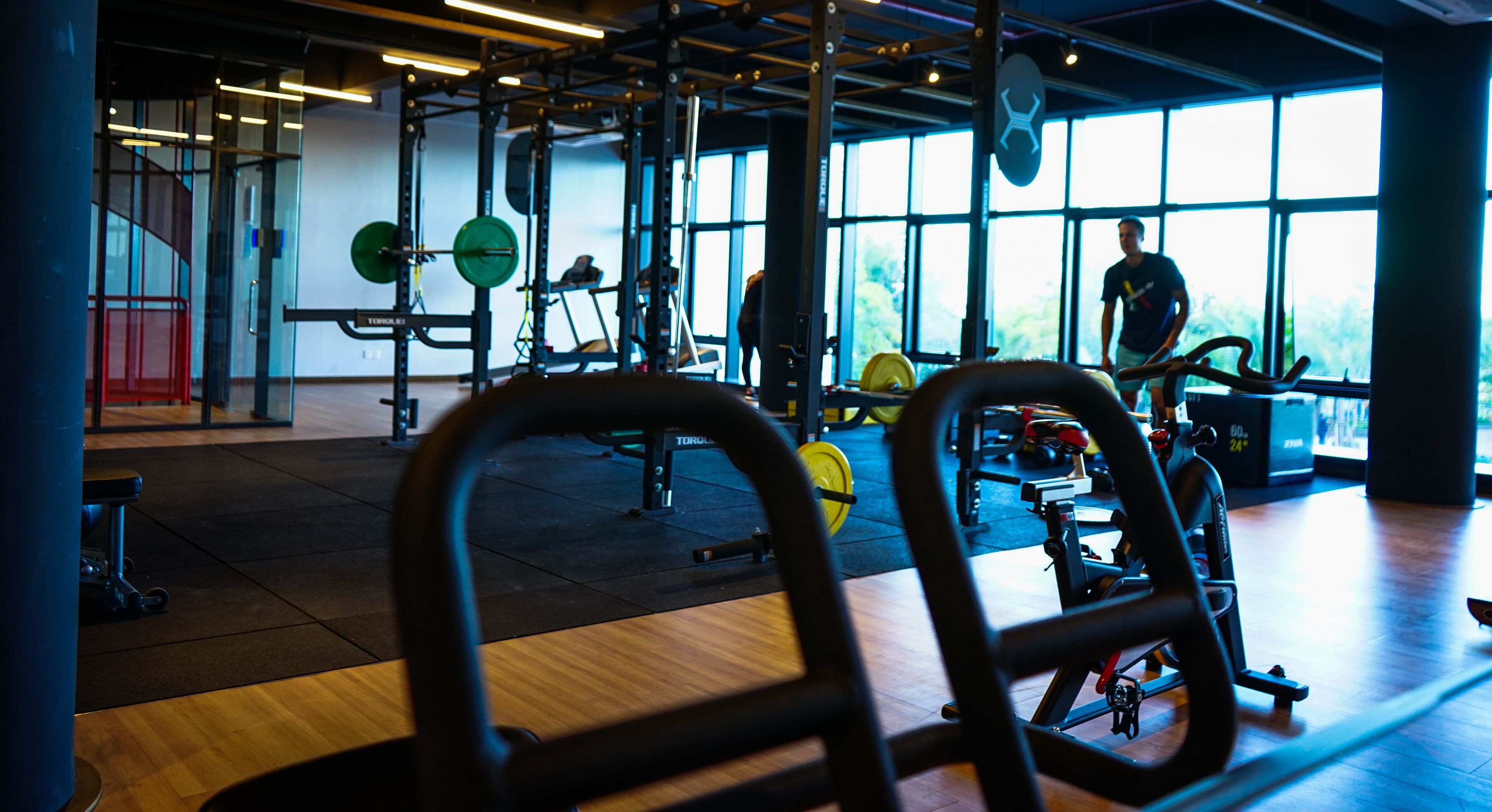 Un gimnasio con equipo de levantamiento de pesas, amplias ventanas y suelo de madera.