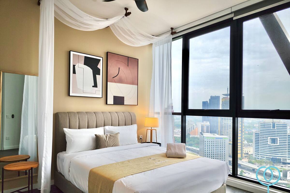 A hotel room with a large bed, a city view, and two framed artworks on the wall.