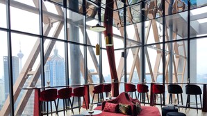 A modern interior with a red sofa, black ottomans, and red chairs. A large window offers a view of a cityscape with a distinctive tower. - Scarletz Suites KLCC by Mykey (Kuala Lumpur)