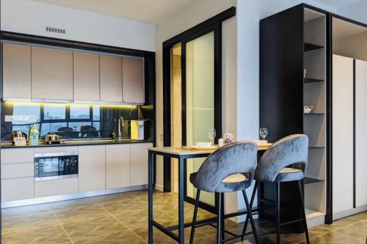 A modern kitchen with a dining area, featuring a built-in oven, a sink, and a countertop with various items.
