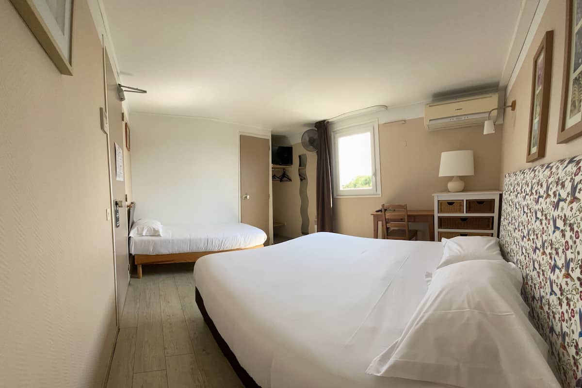 Una habitación de hotel con dos camas individuales, un escritorio, una silla, un armario y un ventanal con cortinas.