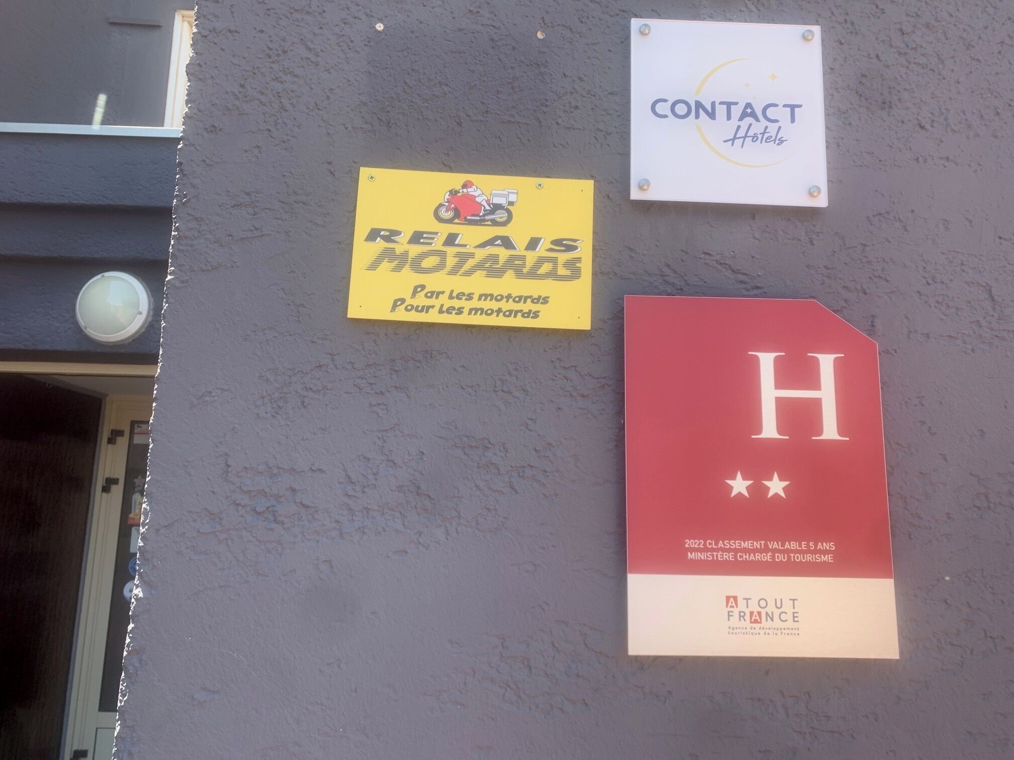 Una pared con tres letreros: un letrero amarillo con una motocicleta y texto, un letrero blanco con una luna creciente y estrellas, y un letrero rojo con una 'H' mayúscula y estrellas.