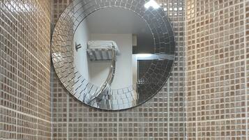 A bathroom with a round mirror, a sink, and a hand dryer.