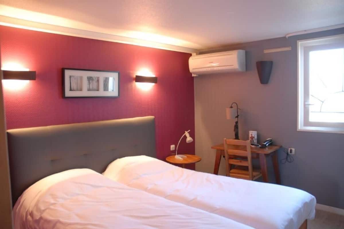 Habitación de hotel con cama, escritorio, silla, lámpara y aire acondicionado instalado en la pared.