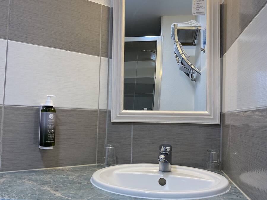 Un bagno con lavandino bianco, uno specchio e un erogatore di disinfettante per le mani.