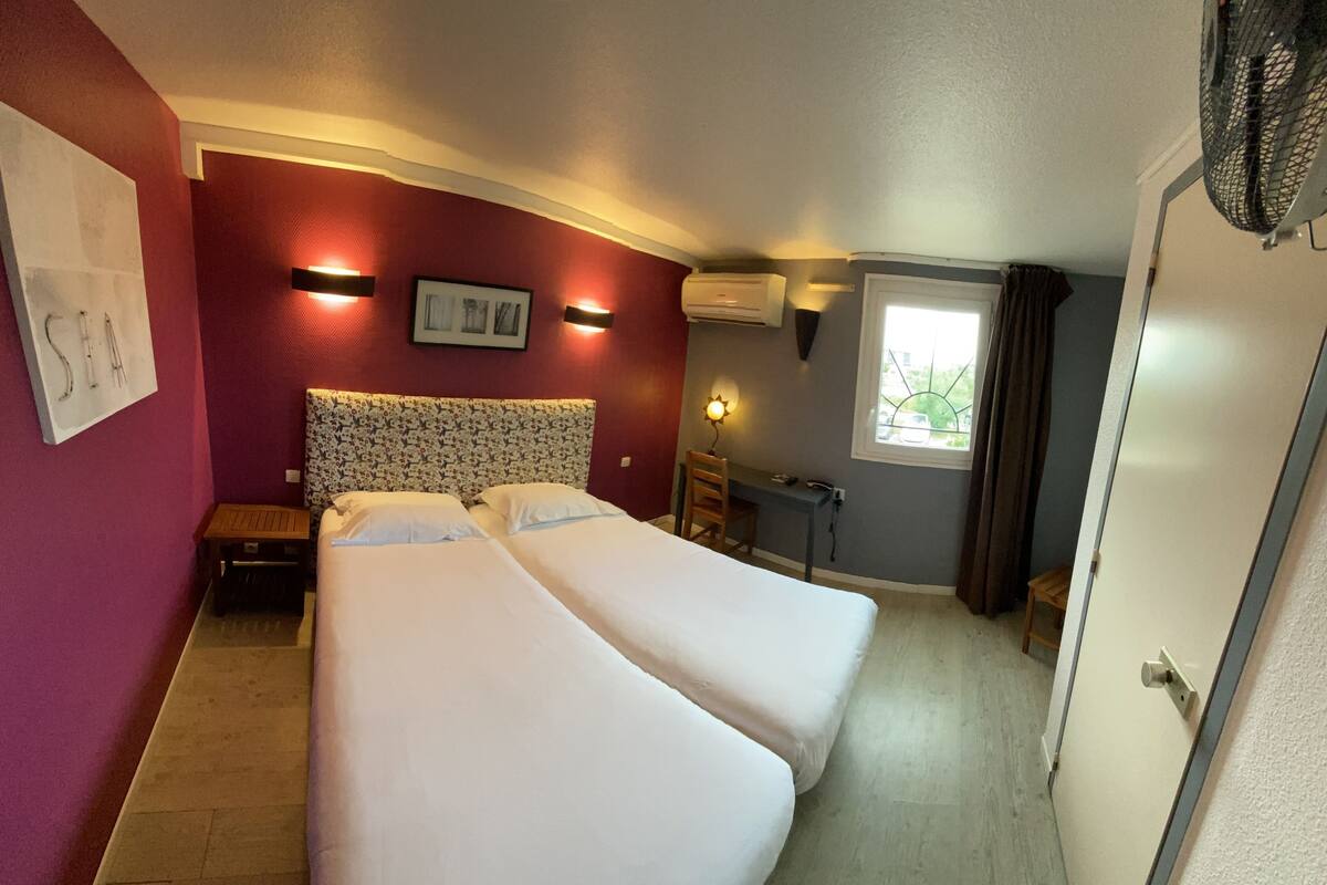 Habitación de hotel con dos camas, un escritorio, una silla, una ventana con cortinas y una puerta.