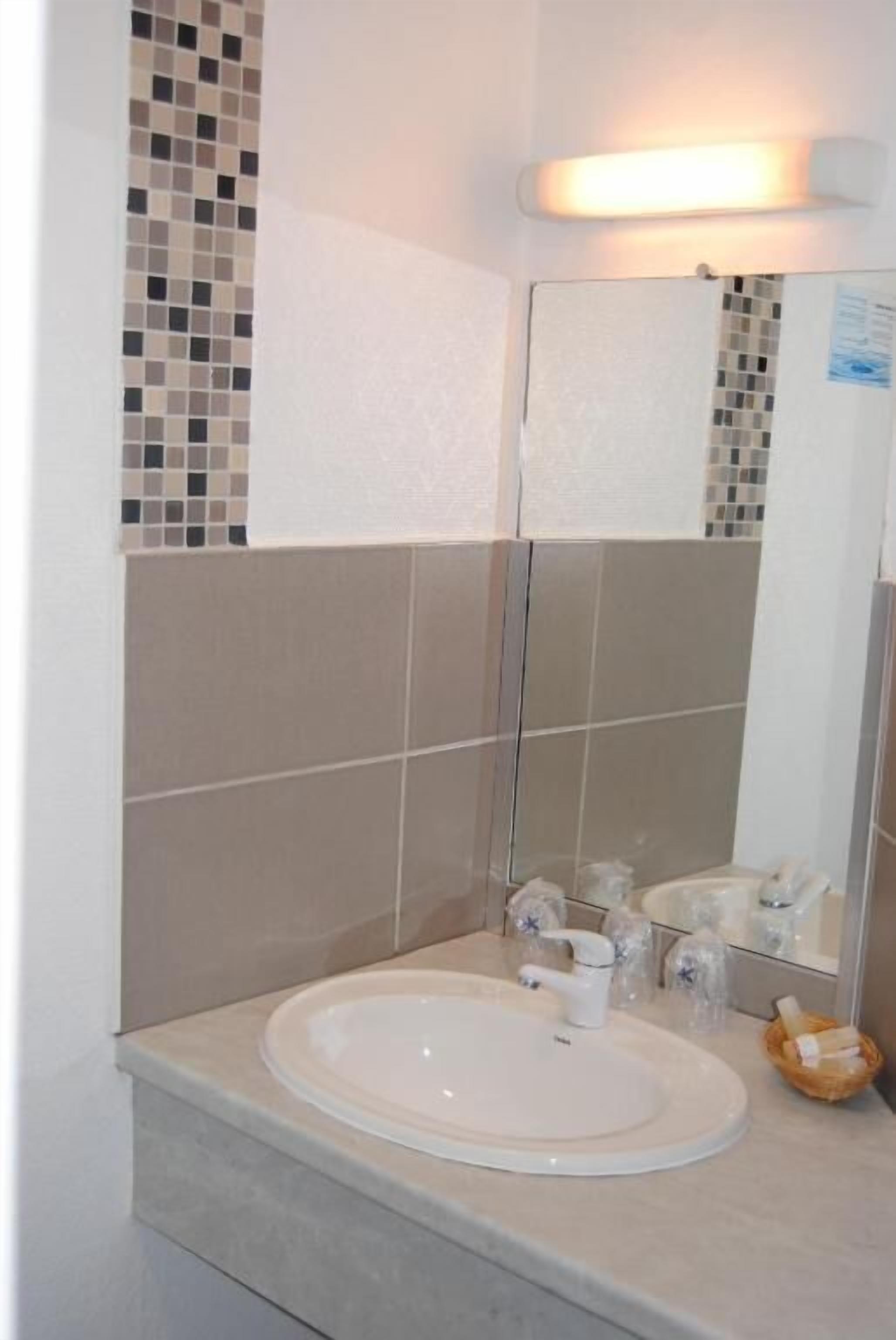 Un baño con lavamanos blanco, espejo y paredes de azulejos.