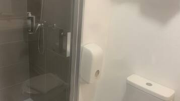 Een badkamer met een douchecabine van glas, een toilet en een zeepdispenser.
