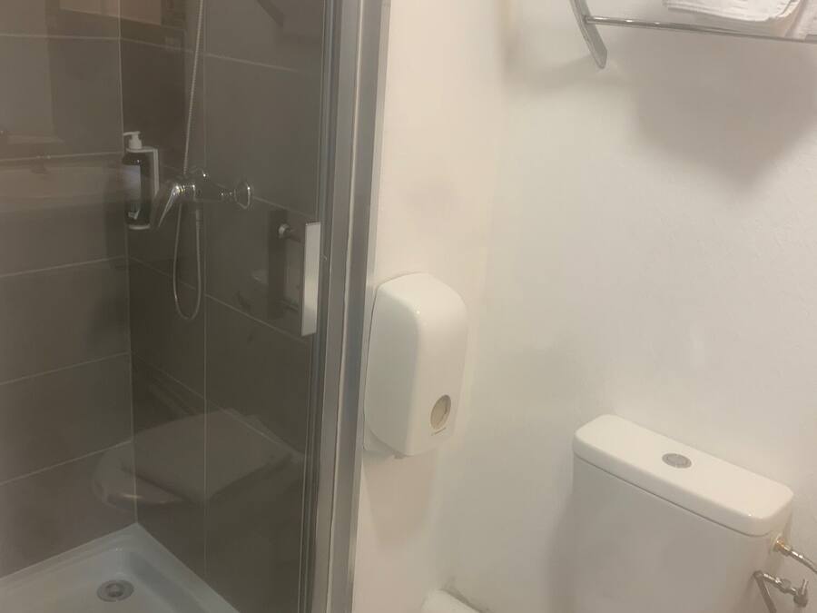 A bathroom with a glass-enclosed shower, a toilet, and a soap dispenser.