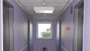 A narrow hallway with purple walls, a window at the end, and a door on the left. - Le Sud Hotel (Mauguio)