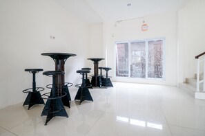A room with multiple bar stools arranged in a row, a large window with a view of trees, and a staircase leading to an upper level. - Urbanview Hotel AVA Banjarmasin (Banjarmasin)
