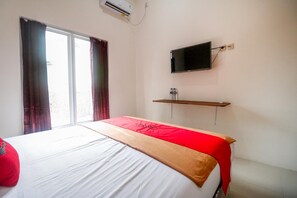 Habitación de hotel con cama, televisor montado en la pared y ventana con cortinas.