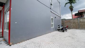 A building with a grey exterior, a red-framed entrance, and a paved area with a parked motorcycle.