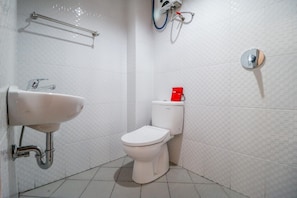 Un baño con inodoro blanco, lavamanos instalado en la pared y secamanos.