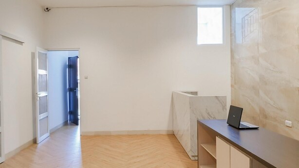 A spacious room with a wooden floor, a marble wall, a desk with a laptop, and a window. - Reddoorz Near Istana Plaza 3 (Bandung)