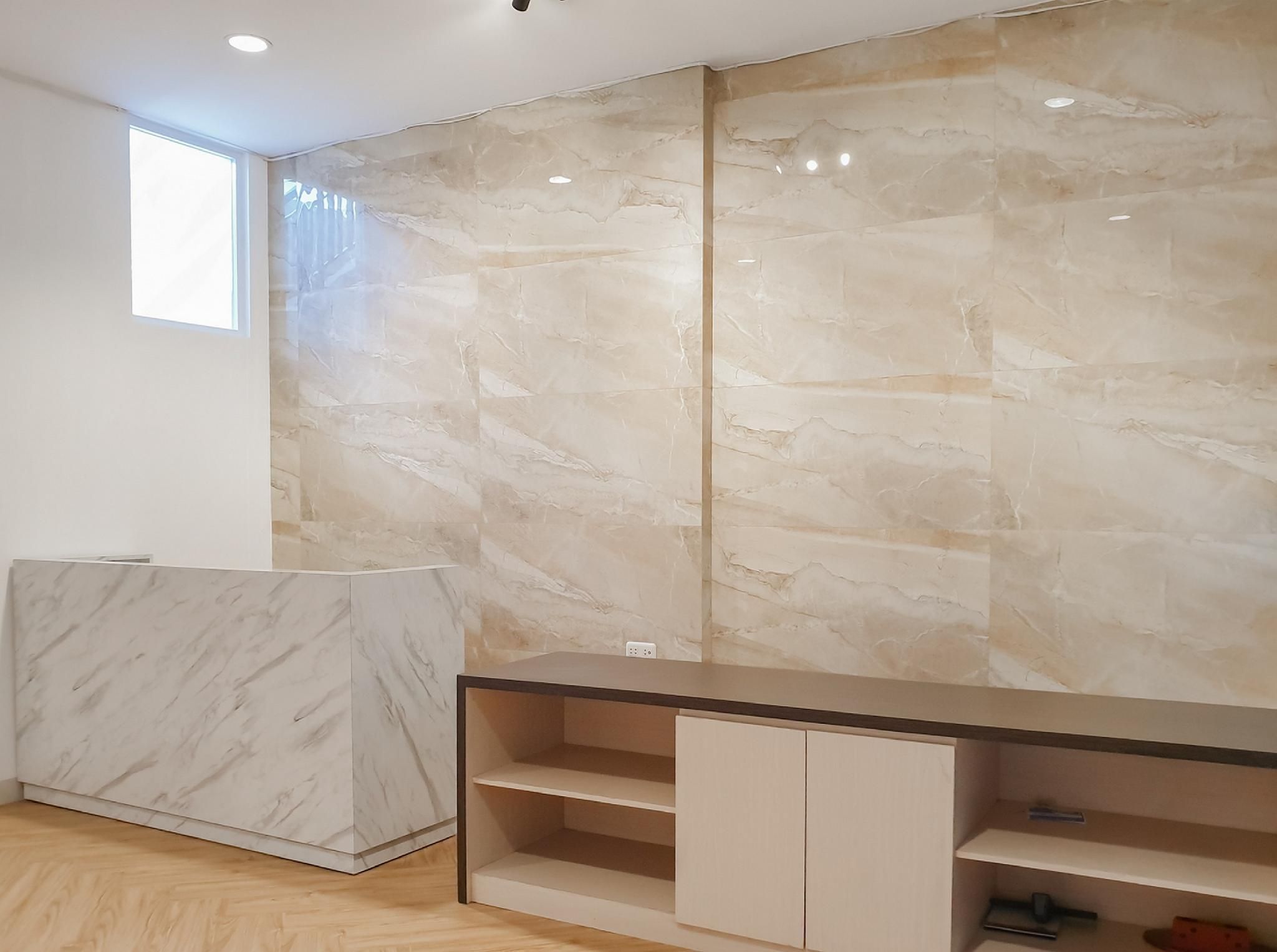 A modern room with a marble wall, a wooden floor, and a built-in desk with shelves.