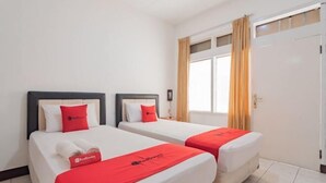 Habitación de hotel con dos camas, cada una con una manta y almohada rojas, y una ventana con cortinas.