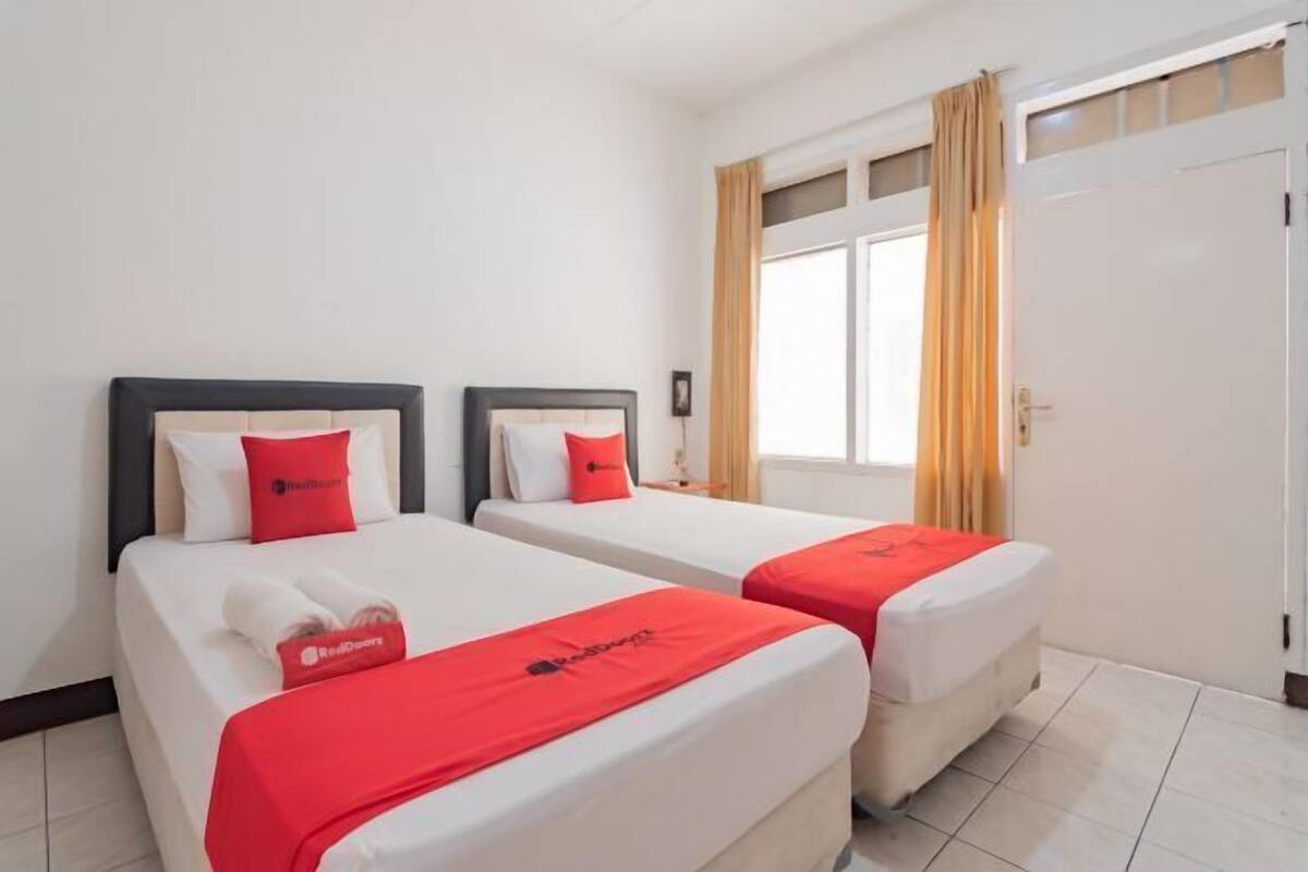 Une chambre d’hôtel avec deux lits, chacun recouvert d’une couverture et d’un oreiller rouges, et une fenêtre avec des rideaux.