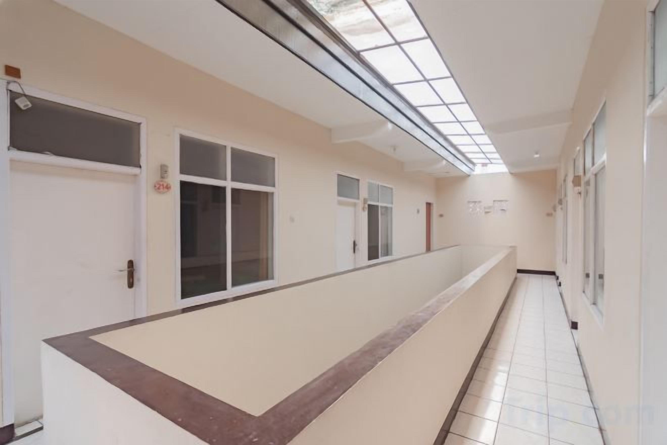 A long corridor with doors on one side and windows on the other, leading to rooms.