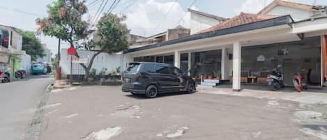 A parking area with a car and a motorcycle, a covered outdoor seating area, and a building with a tiled roof.