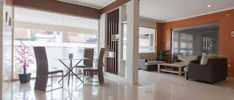 A modern hotel lobby with a glass partition, a seating area with a sofa and chairs, and a large window offering a view of the outside.
