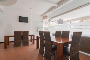 Un salón de conferencias con una larga mesa y sillas, un televisor de pantalla plana en la pared, y un amplio ventanal con vistas a edificios.