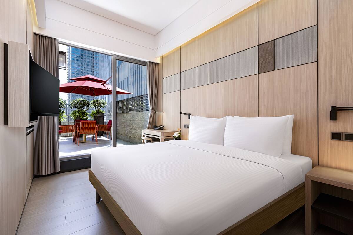 Une chambre d’hôtel moderne dotée d’un grand lit, d’une télévision, d’un bureau et d’un balcon avec coin salon extérieur.