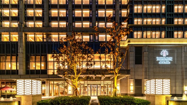 Fachada de hotel con ventanas iluminadas, una entrada central y un letrero que indica que es un hotel.