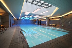 Una amplia piscina interior con suelo de baldosas, barandilla de cristal y tragaluz.