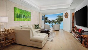 Una sala de estar moderna con un sofá, una mesa de centro y un mueble para televisión. Hay un cuadro grande en la pared y vista al océano a través de la ventana.
