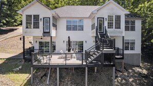 A two-story white house with a deck, a staircase, and a front door. - Eagles Landing - Lakefront 5 Bdrm with Lakeside Tiki Bar (Sunrise Beach)