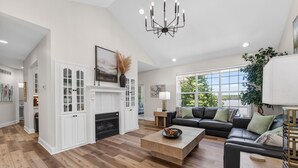 A spacious living room with a fireplace, a black leather sofa, and a wooden coffee table. - Eagles Landing - Lakefront 5 Bdrm with Lakeside Tiki Bar (Sunrise Beach)
