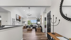 A spacious living area with a wooden floor, a sofa, a coffee table, and a dining table. - Eagles Landing - Lakefront 5 Bdrm with Lakeside Tiki Bar (Sunrise Beach)