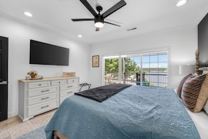 Une chambre à coucher avec un lit, un ventilateur de plafond, une télévision, une commode et une fenêtre donnant sur un beau paysage.