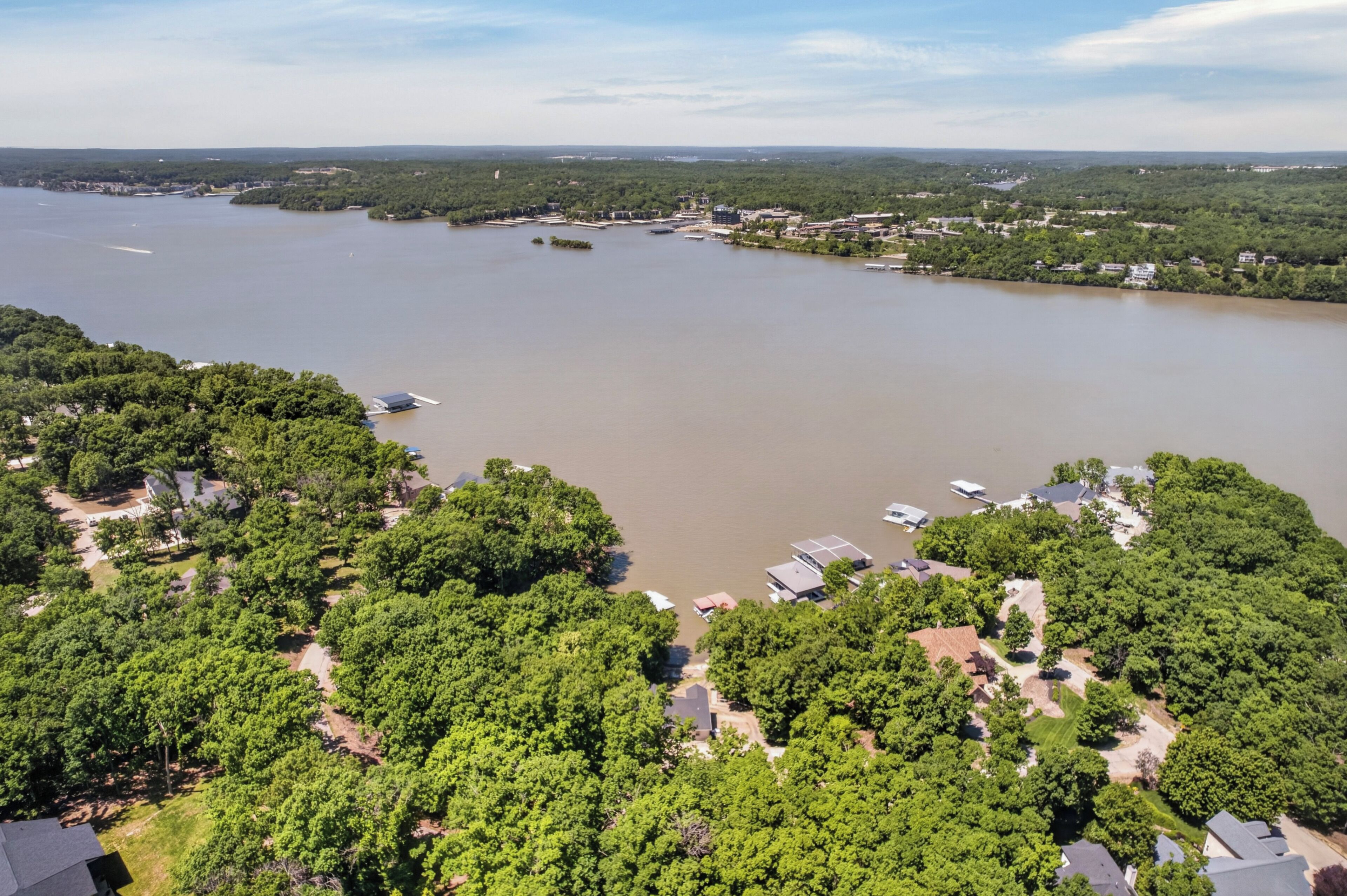 A river with boats, surrounded by dense green trees and buildings.