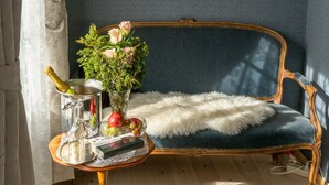 Une pièce avec un mur bleu, un tableau encadré, un canapé, une petite table ronde avec une bouteille, un vase de fleurs et un tapis en fourrure.