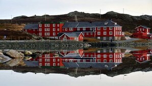 Un bâtiment rouge doté de nombreuses fenêtres et d’un toit plat, situé près d’une étendue d’eau dont le reflet est limpide.