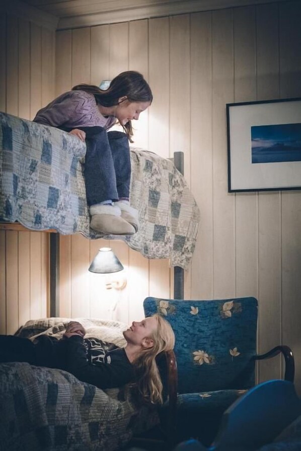 A room with two bunk beds, a framed picture on the wall, and a lamp on the nightstand.