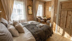 Une chambre confortable avec un grand lit, un fauteuil et une petite table sur laquelle est posé un vase.
