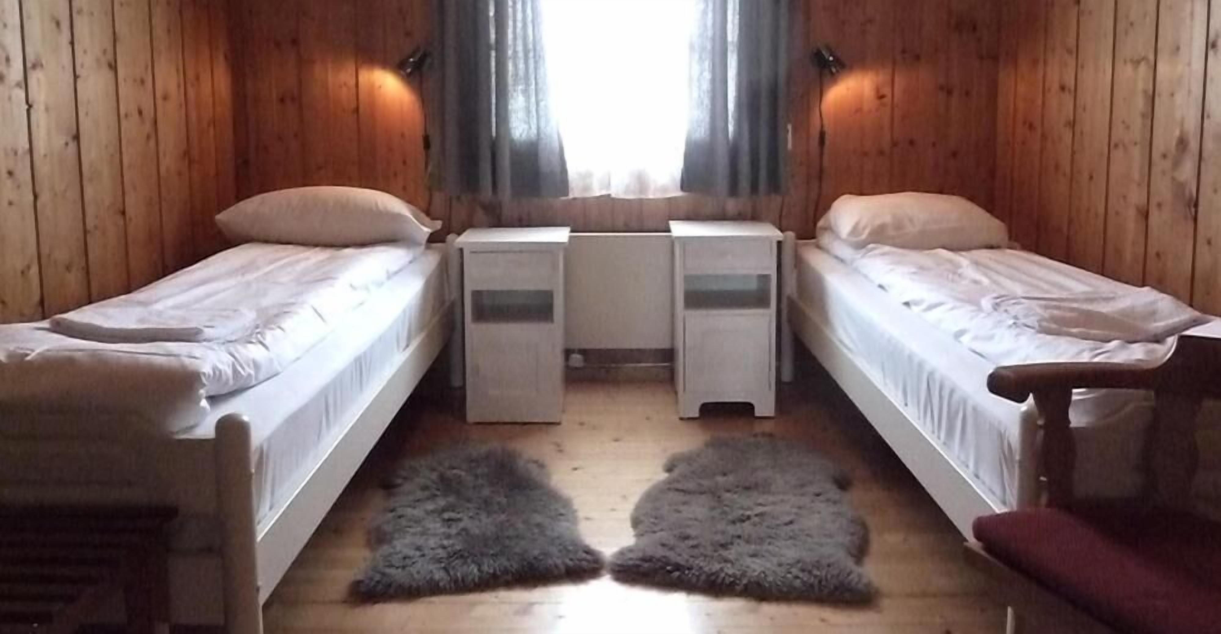 Habitación tipo cabaña con dos camas individuales, una mesita y una silla.