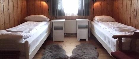 Habitación tipo cabaña con dos camas individuales, una mesita y una silla.