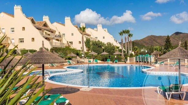 A swimming pool with lounge chairs and umbrellas, surrounded by buildings with unique architecture. - La Manga Club Los Olivos Apartment 593 (La Manga Club, Cartagena)