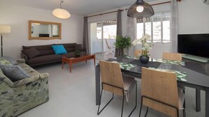 Ein modernes Wohnzimmer mit Sofa, Couchtisch, Esstisch, Stühlen und einem Fernseher.