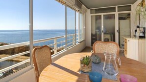 Ein Balkon mit Meerblick, ein runder Holztisch mit Stühlen und eine Küchenzeile im Hintergrund.