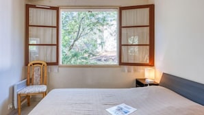A bedroom with a bed, a chair, a window with curtains, and a nightstand with a lamp. - Dominique by Interhome (Lacanau)